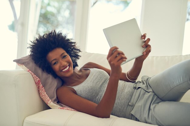 Saturdays are lazy days Portrait of a young woman using her digital tablet while relaxing at home