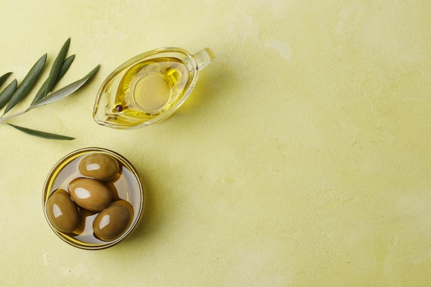 Salsiera con olio d'oliva, olive verdi e foglie su sfondo verde, vista dall'alto