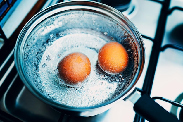 Ciotola in acciaio inossidabile con uova bollenti colazione in acqua su una stufa a gas