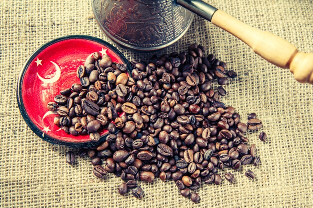 Saucer with elements of turkish flag, coffee beans and copper\
coffee pot on sack cloth