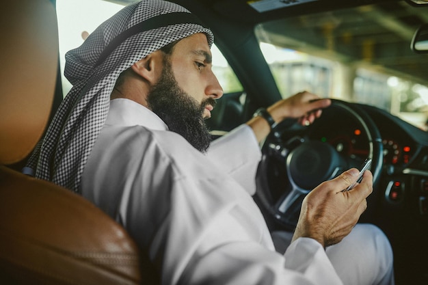 Uomo saudita seduto in macchina e parlando al telefono