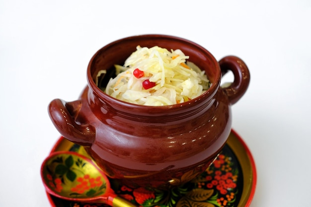 Sauerkraut in a clay pot on wooden Khokhloma plate and spoon isolated on white