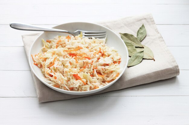 Sauerkraut at white rustic wood. Appetizer cabbage with carrot in plate.