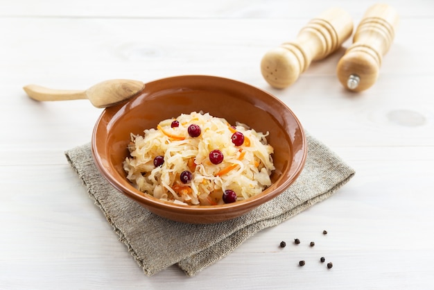 Sauerkraut with cranberries in a clay bowl with a wooden spoon