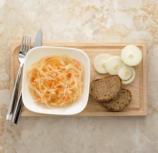 Sauerkraut with onion and bread on a wooden board.