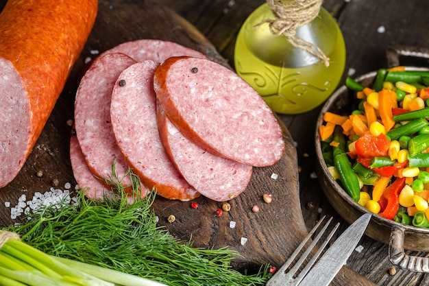 sausage cervelat or salami, whole and slices, lies on a wooden rustic table or background, cutting