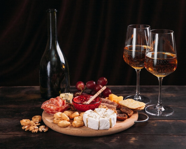 Sausage and cheese cut on round board with fruit cookies and sauce with two glasses of white port and a bottle