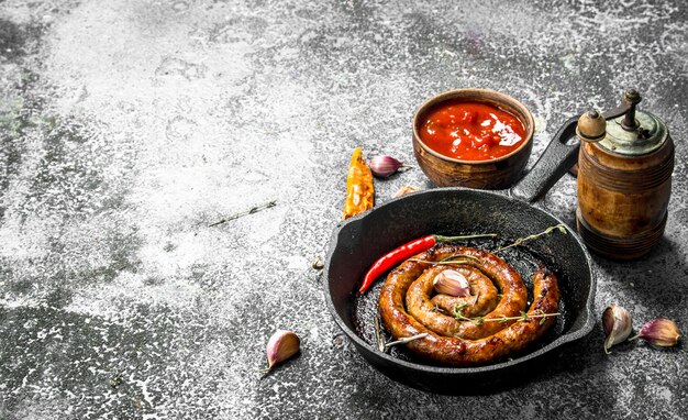 Sausage in a frying pan with hot peppers, garlic and sauce on rustic table.