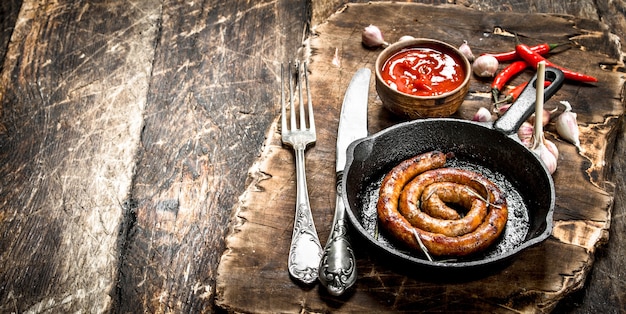 Sausage in a frying pan with tomato sauce and garlic on a wooden background