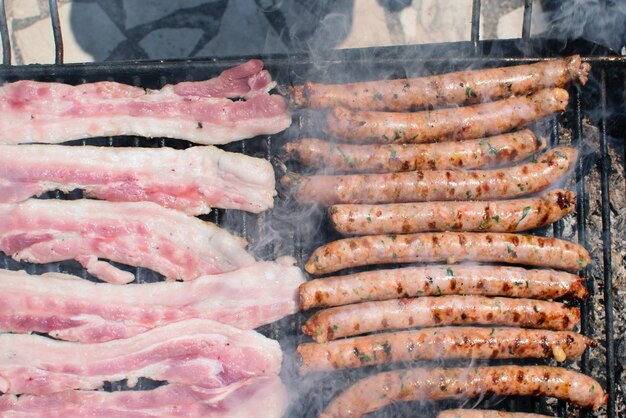 Sausages and bacon cooking on smoking barbecue on terrace