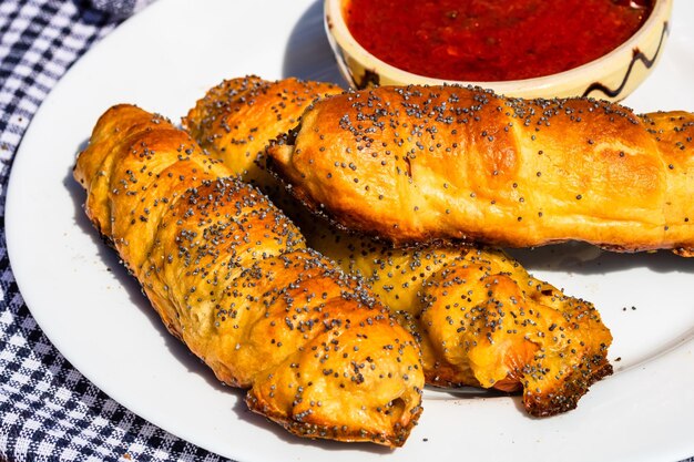 Sausages baked in dough sprinkled with salt and poppy seeds and bowl with tomatoes sauce in a rustic composition sausages rolls delicious homemade pastries