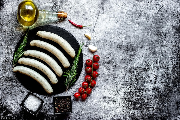 Sausages on a black plate with olive oil and garlic on a gray background.