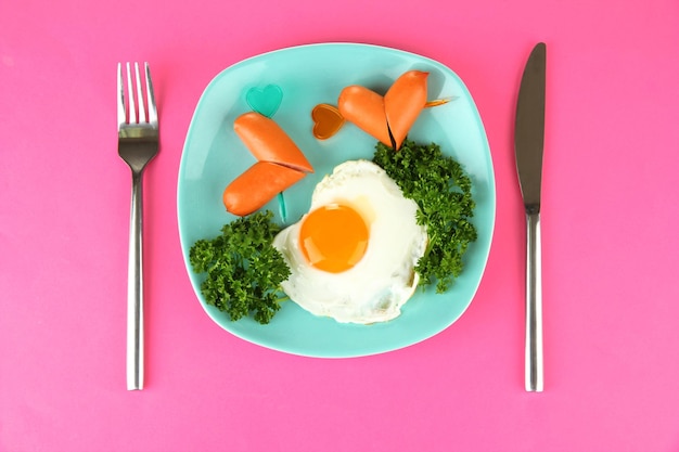 Sausages in form of hearts, scrambled eggs and parsley, on color plate, on color background