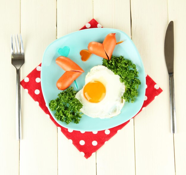 Sausages in form of hearts, scrambled eggs and parsley, on color plate, on wooden background