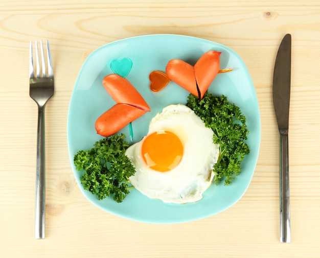 Sausages in form of hearts, scrambled eggs and parsley, on color plate, on wooden background