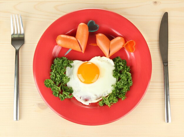 Sausages in form of hearts, scrambled eggs and parsley, on color plate, on wooden background