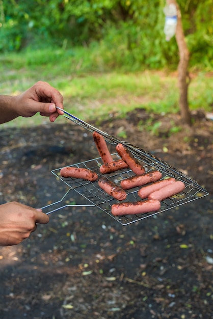 Salsicce alla griglia sul fuoco. la mano dell'uomo rimuove le salsicce dalla griglia