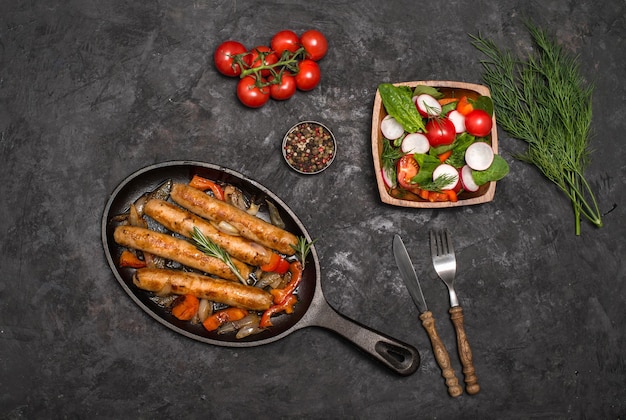 Sausages on the grill pan on the wooden background Top view Frying pan with fried sausage vegetables and fork and knife on a rustic wooden table