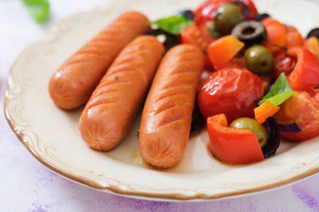 Photo sausages grilled with vegetables in the greek style on plate.