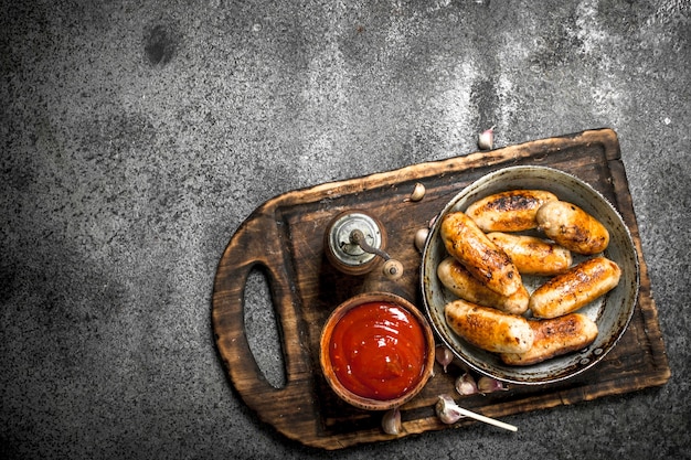 Sausages with tomato sauce on board on rustic table.