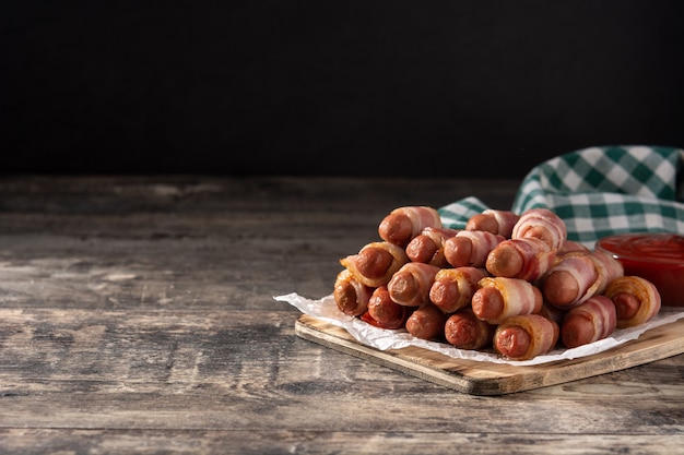 sausages wrapped in smoked bacon on wooden table