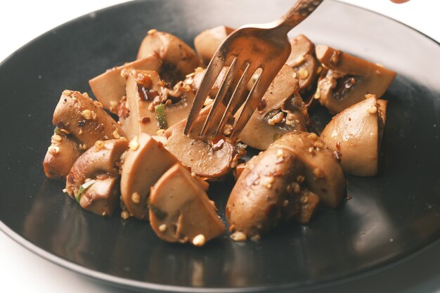 Sauteed mushrooms with garlic and parsley on a black plate on white surface