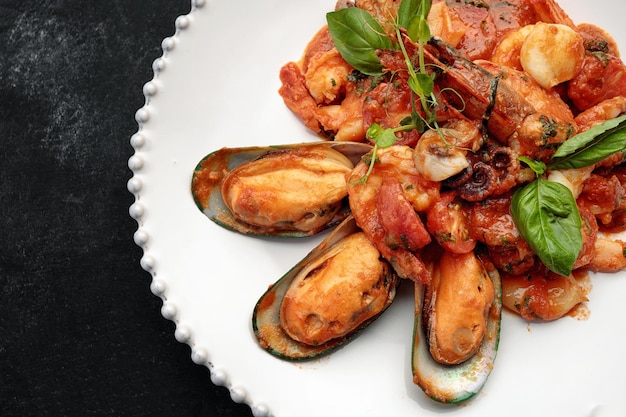 Жареные морепродукты с креветками, мидиями, кальмарами и гребешком на белой тарелке на темном фоне