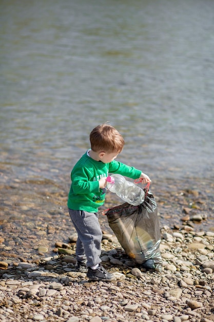 環境を守るコンセプト 砂浜でゴミとプラスチックのボトルを集め ゴミ箱に捨てる小さな男の子