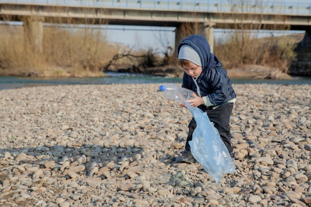 Save environment concept, a little boy collecting garbage and plastic bottles on the beach to dumped into the trash.