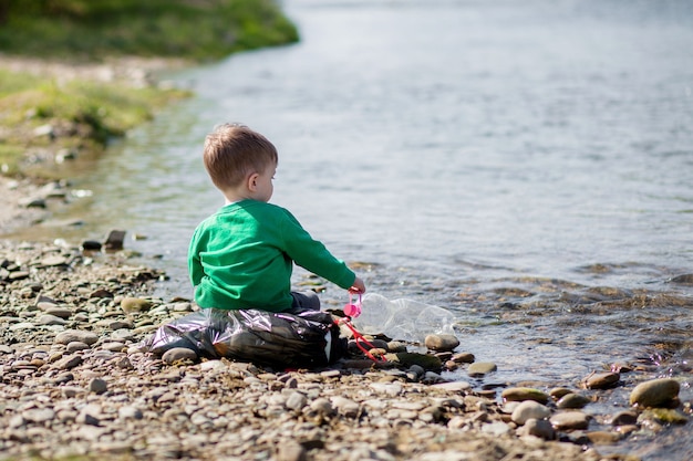 Save environment concept, a little boy collecting garbage and plastic bottles on the beach to dumped into the trash.