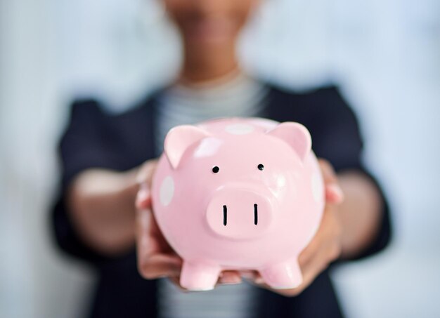 Save money and become financially independent Cropped shot of an unrecognizable businesswoman holding a piggy bank inside her office