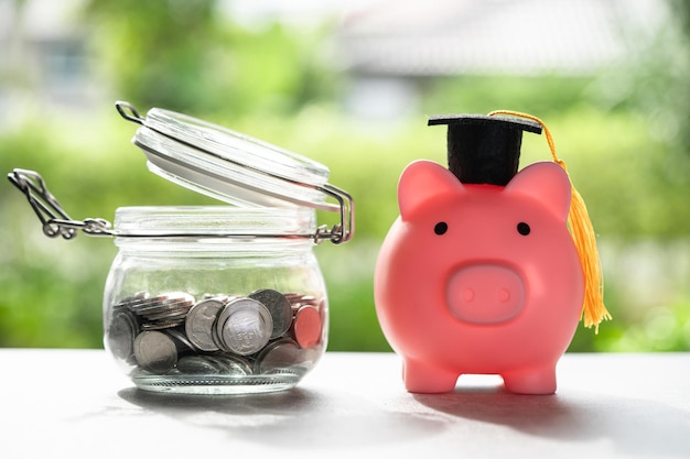 Save money coins in grass jar with piggy bank and graduation cap Business finance education concept