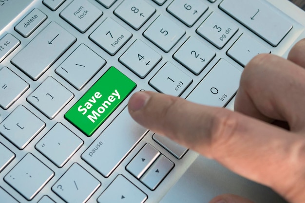コンピューターのキーボードの青いボタンで投資コンセプトのお金を節約します。男性の指が現代のラップトップの灰色の銀色のキーボードのカラーボタンを押します。碑文のあるボタンをクローズアップ。