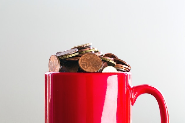 Saved Money in a colorful red mug to Finance Goals overflowing with euro coins, business concept