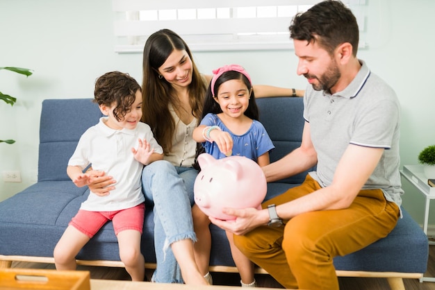 Saving as a family. Attractive mom, dad and little children putting money on a piggy bank and trying to save to take a family vacation