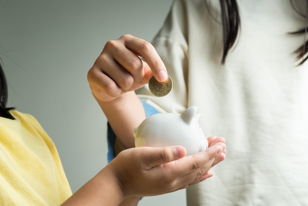 Saving and business concept, two little girl with piggy bank and coins at home