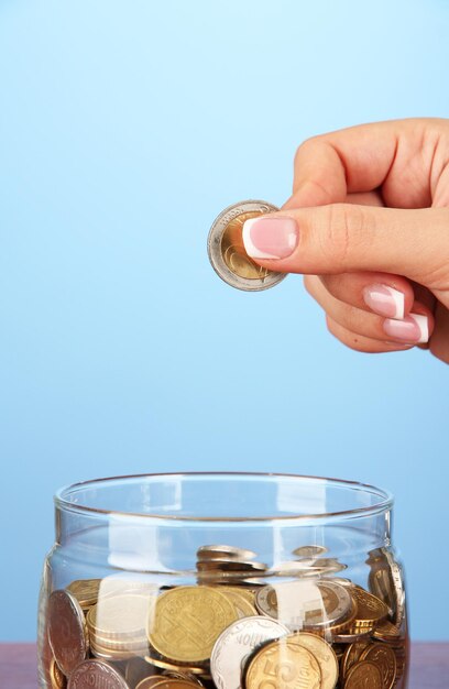 Saving female hand putting a coin into glass bottle on color background
