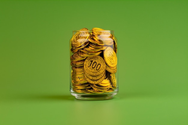 Saving gold coins in glass jars on green background coin savings concept