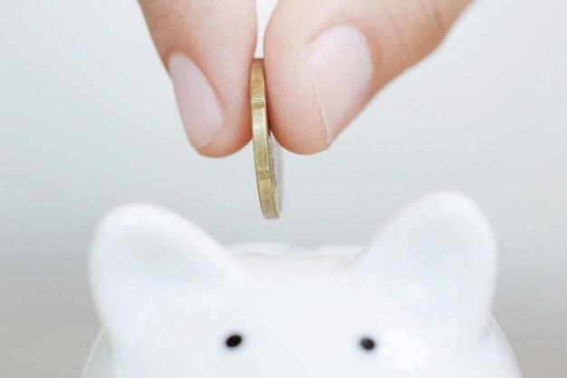 Saving, hand putting golden coin in piggy bank money box white.