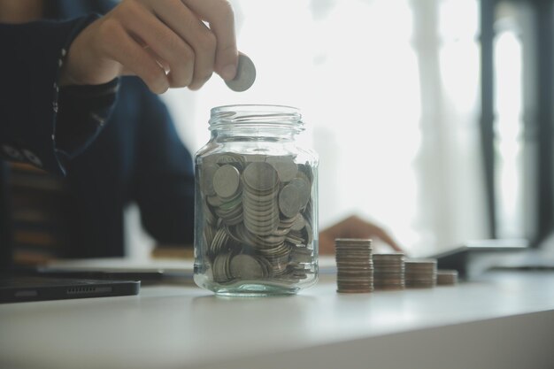 Photo saving money and accounting concept business man putting coin insert to jar and make acounting book for finance management to investment and saving