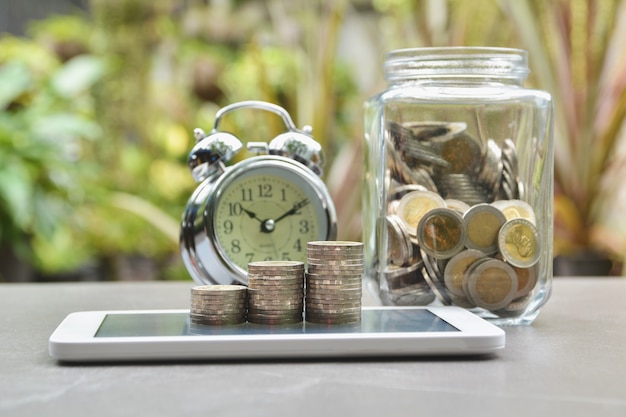 Saving money concept with money coin stack on smart-phone and alarm clock