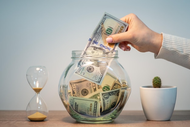 Saving money in glass bank Hand of a woman putting dollar banknote to the jar saving money