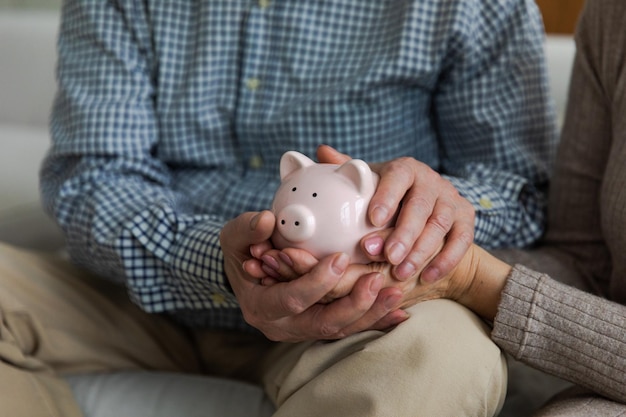 Saving money investment for future senior adult mature couple hands holding piggy bank with money co