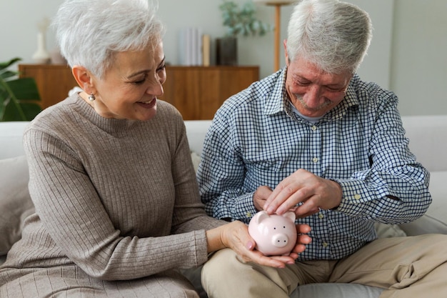 Saving money investment for future senior adult mature couple holding piggy bank putting money coin