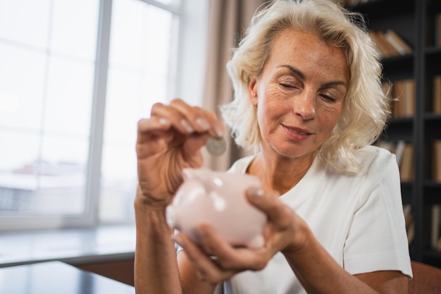 Photo saving money investment for future senior adult mature woman putting money coin in piggy bank old