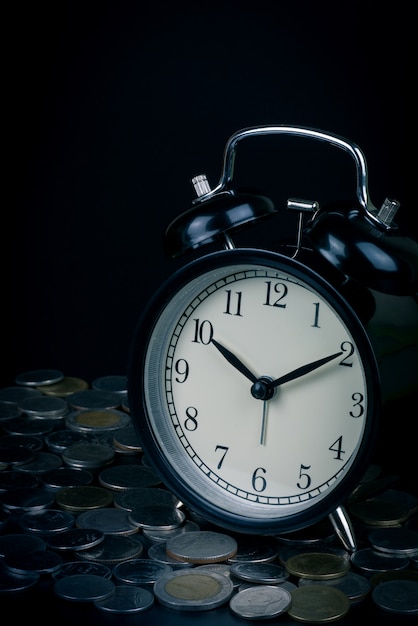 Photo saving time, alarm clock standing with coins isolated on black