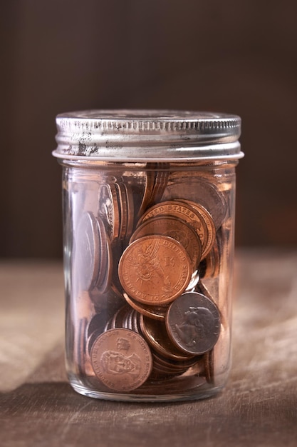 savings of coins deposited in a glass jar (dollar), on a wooden base. Investment and savings concept