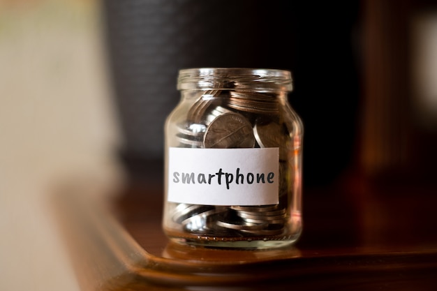 Концепция сбережений для смартфона - стеклянная банка с монетами и надписью.