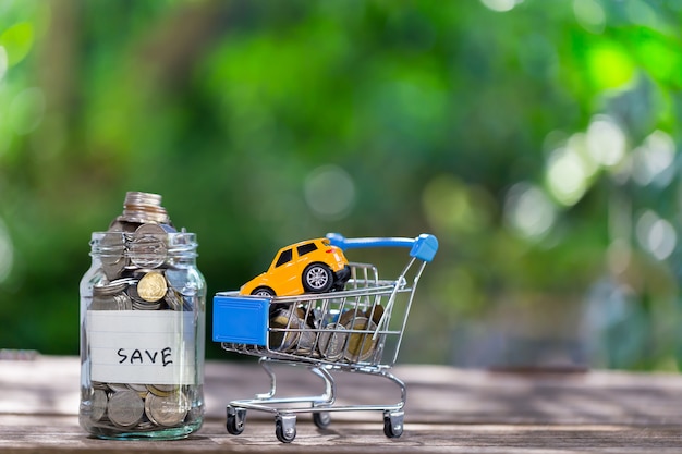 Savings deposit coins in a clear glass bottle, on a wooden floor with bokeh in the background.