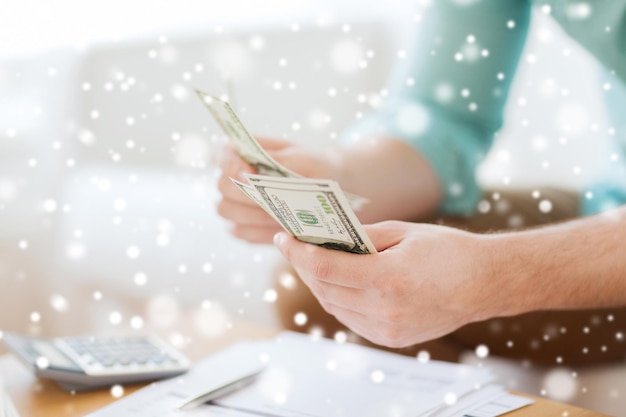 savings, finances, paperwork and people concept - close up of man counting money and making notes at home